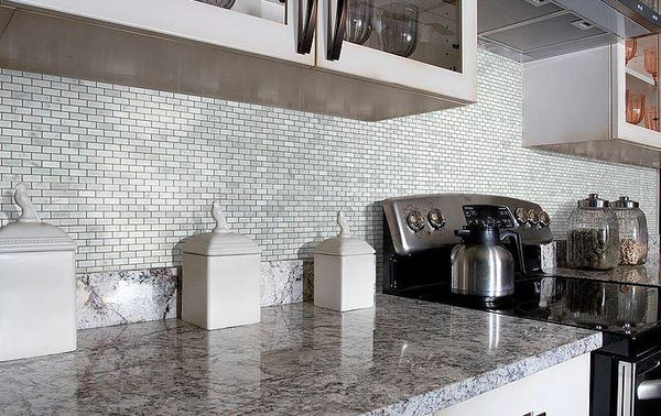 Marble countertops and silver stove against mini brick mosaic tile wall in kitchen