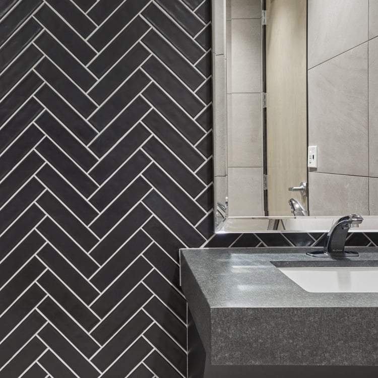 Black matte handmade look wall tile set in herringbone behind a vanity