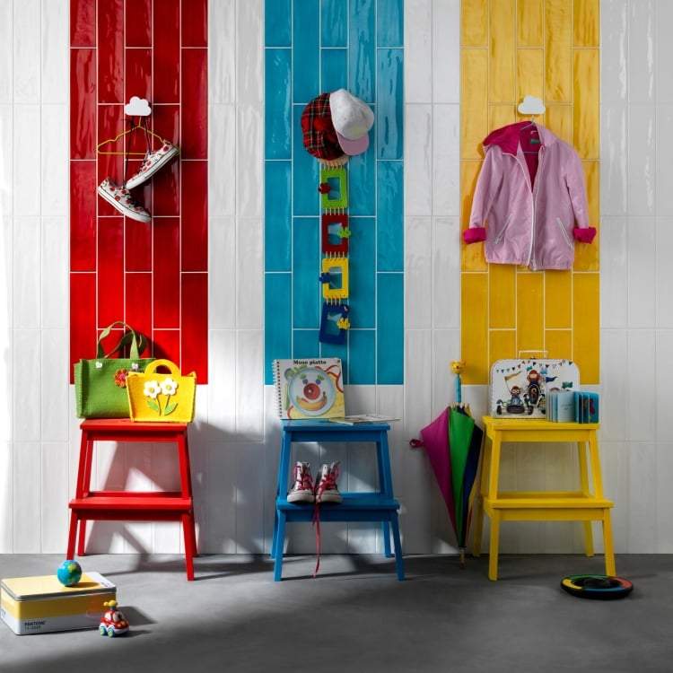 4x16 Gioia tile in bright red, blue, and yellow on a wall between white tile. The room features a colorfull classroom setting for kids.